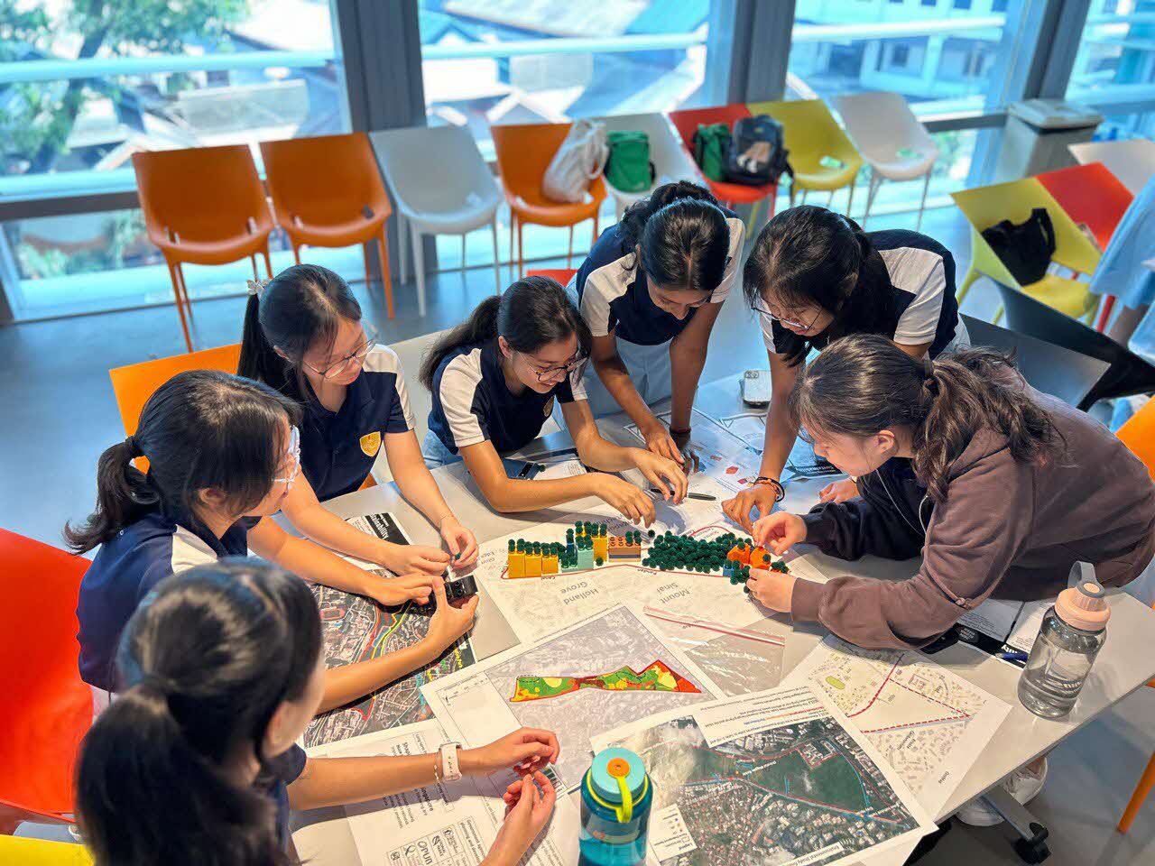 Students collaborating in a hands-on urban planning activity, using maps and building blocks to design and develop a city layout.